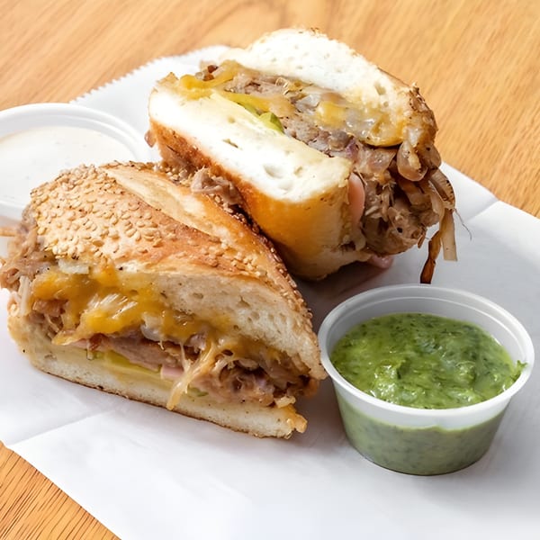 Andale Latino Grill's Latin-American sandwich, cut in half, with melted cheese, onions, and two dipping sauces.