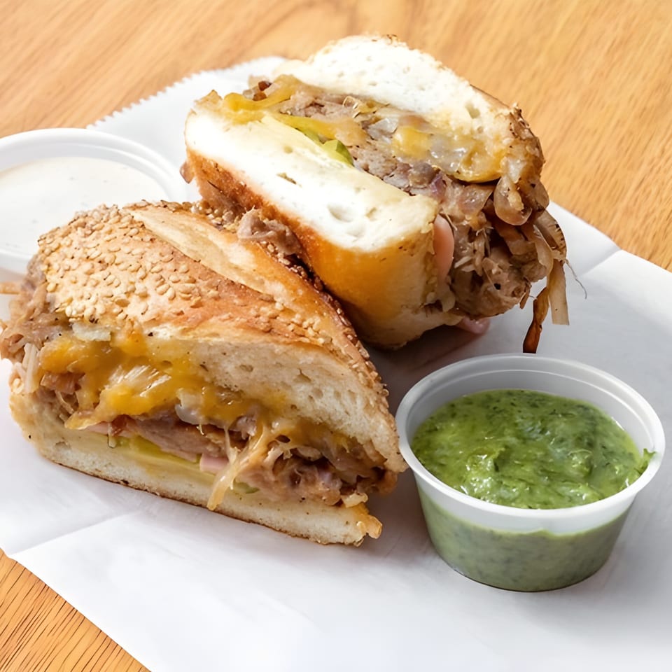 Andale Latino Grill's Latin-American sandwich, cut in half, with melted cheese, onions, and two dipping sauces.
